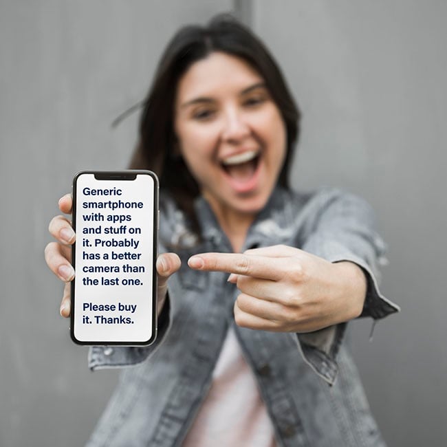 Young woman holding up a generic smarphone, pointing to it and smiling.